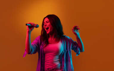 Caucasian female singer portrait isolated on orange studio background in neon light. Beautiful...