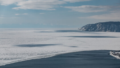 Obraz premium There is a clear border between the white ice of Lake Baikal and the blue water of the non-freezing Angara River. Mountain range against the sky. Siberia.