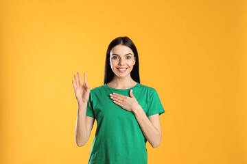 Attractive young woman showing hello gesture on yellow background