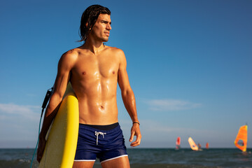 Portrait of handsome surfer with his surfboard. Young man with a surfboard on the beach