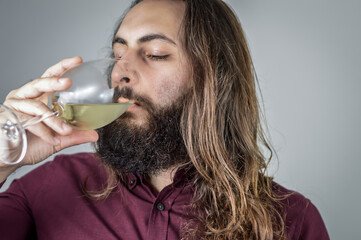 portrait of a young middle eastern businessman with beard and long hair drinking a glass of fresh white wine