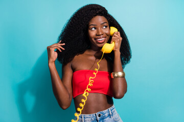 Photo of dreamy charming afro american lady look empty space hold telephone isolated on teal color...