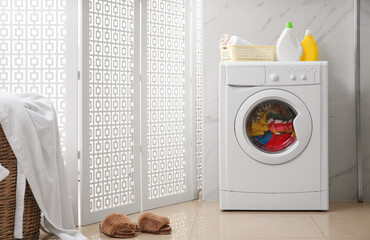 Modern washing machine with clothes in bathroom
