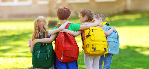 Group of children with rucksacks standing in the park near the school - obrazy, fototapety, plakaty