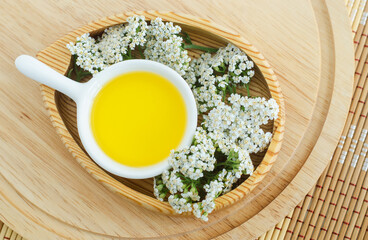 Small white bowl with cosmetic (cleansing) aroma oil and white yarrow flowers. Natural skin care, homemade spa and beauty treatment recipe. Top view, copy space.