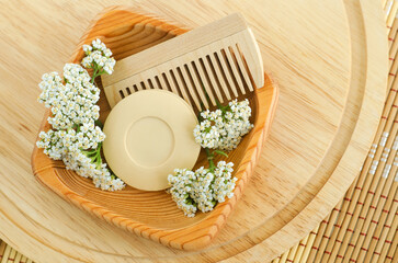 Small bowl with herbal bar of soap (solid shampoo), yarrow flowers and wooden hairbrush. Aromatherapy, spa and natural hair care. Flat lay, copy space