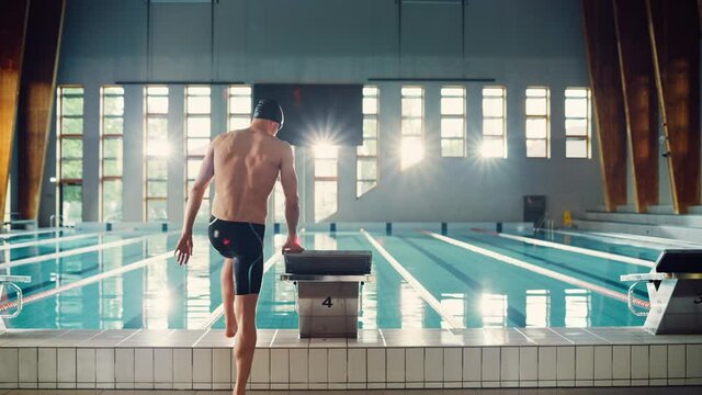 Athletic Male Swimmer Comes to Starting Block and Jumps Divining into Swimming Pool. Determined Professional Athlete Training for the Championship. Cinematic Light. Following Slow Motion Shot