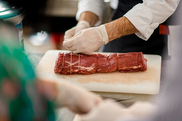 Close-up view of meat and chef's hands which tie it with butcher's twine