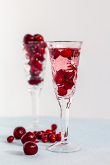 a crystal glass of pink gin or vodka infused with cranberry on light background, berry liquor or any alcohol cocktail among red berries, cranberries and cherries on crystal sherry goblet, minimalism