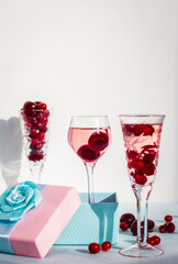set of glasses of pink gin or vodka infused with cranberry among frozen berries, a long-stemmed glass with cherry liqueur or any red alcoholic cocktail standing in gift box