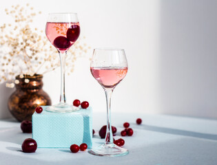 a pair of glasses of pink gin or vodka infused with cranberry among frozen berries, a long-stemmed glass with cherry liqueur or any red alcoholic cocktail standing on blue box base, copy space