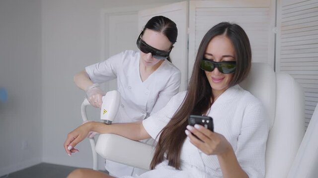 During a laser hair removal session, a woman in a beauty salon writes a message in her mobile phone. Hand hair removal photo hair removal and a woman writes a message in a smartphone