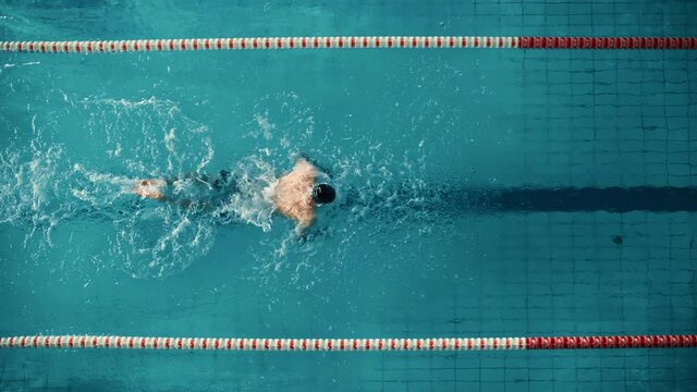 Aerial Top View Male Swimmer Swimming in Swimming Pool. Professional Athlete Training for the Championship, using Butterfly Technique, Effort and Determination to Win. Cinematic Wide Tracking
