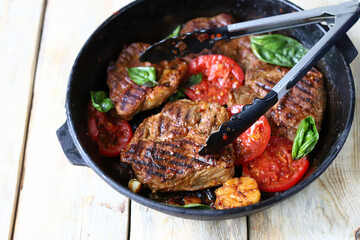 Juicy appetizing grilled steak. Tongs for meat and a frying pan with steaks.