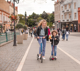 Obraz premium The happy mom and daughter are standing with scooters in the city