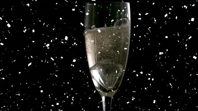 Animation of confetti falling and champagne pouring into glass of champagne on black background