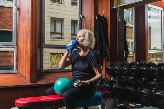 Elderly sportswoman drinking water from bottle during training in gym