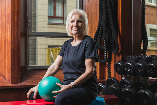 Elderly sportswoman training arms with ball in gym