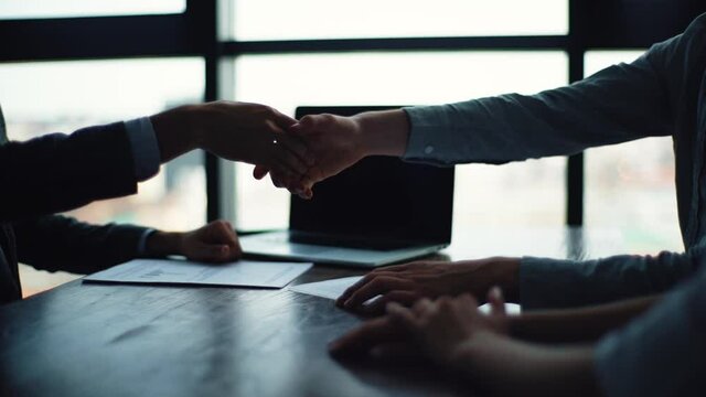 Close-up hands of insurance sale man shake hands with young couple customer after close deal and signed agreement at office. Closeup of happy couple shaking hands with broker on backgrodud of window.