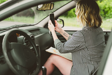 Happy young woman travels by car on the road She looks at the map and phone