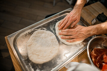 view of male chef's hands who gently adjusts the dough on the baking sheet.