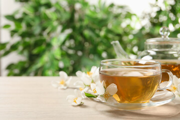 Aromatic jasmine tea and fresh flowers on wooden table, space for text