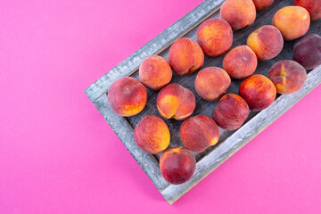 ripe peaches in a wooden box on a pink background