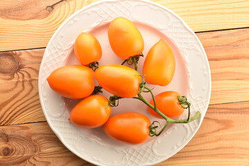 Several juicy yellow plum tomatoes on a white dish, on a wooden table, close-up, top view.