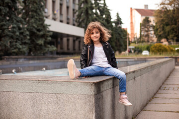 The happy little girl is sitting on a concrete parapet