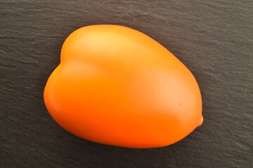 One yellow organic plum tomato on a slate board, close-up, top view.