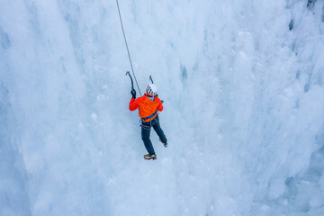 Aerial shot of an ice slope bumps, ridges, and icicles by which climbing up man using traction ice...