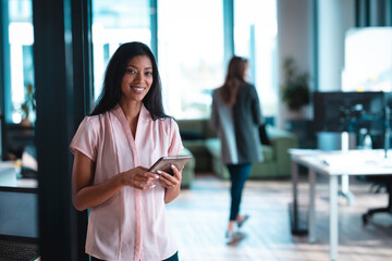 Portrait of mixed race businesswoman smiling and using tablet with colleagues in background