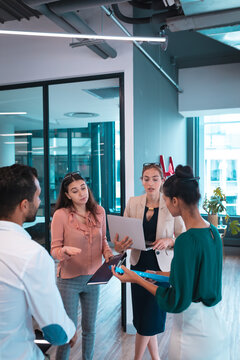 Group of diverse businesspeople discussing together and holding documents and laptop