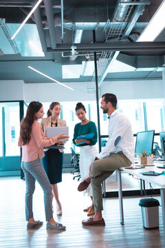 Group of diverse businesspeople discussing together and holding documents and laptop