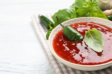Spicy chili sauce with basil on white wooden table, closeup. Space for text