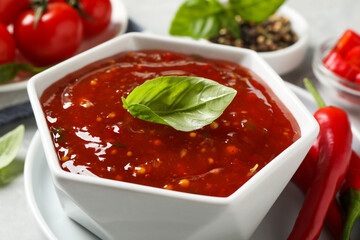 Spicy chili sauce with basil on light table, closeup