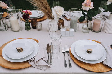 A set of different dishes, cutlery and accessories on a wooden table with a tablecloth - empty plates, forks, knives, glasses, roses in vases, candles in candlesticks.