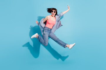 Fototapeta na wymiar Full body profile photo of astonished young lady jump wear top jeans eyewear isolated on blue color background