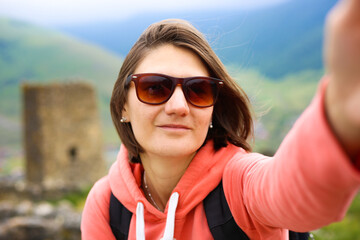 Happy beautiful woman traveller taking selfie and looking at the camera in the mountains.