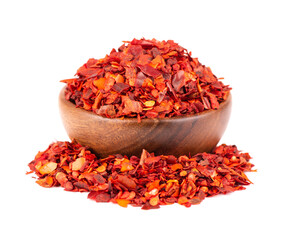 Dried red chili flakes in wooden bowl, isolated on white background. Chopped chilli cayenne pepper....