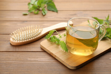 Stinging nettle infusion, leaves and brush on wooden table. Natural hair care