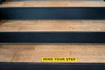 Yellow and black warning sign on wooden stairs is mind your step .Put on your shoes and walk up the stairs,care to be taken when going up or down.