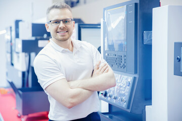 Naklejka na ściany i meble Engineer young man in glasses operates CNC automatic metalworking lathe or laser, industrial worker in modern factory