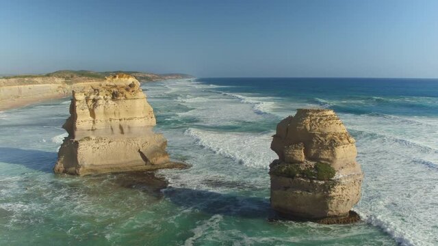 AERIAL: Scenic shot of the famous limestone formations of Twelve Apostles in Victoria, Australia. Golden summer sunshine illuminates the cliffs and promontories of a rugged shoreline in Australia