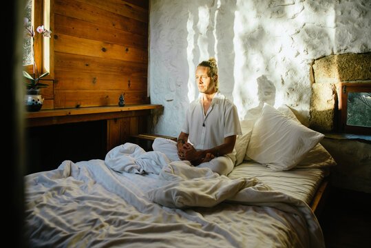 Blond man sitting on a bed while practicing meditation
