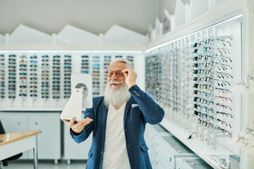Cheerful elderly man trying on glasses in optical store