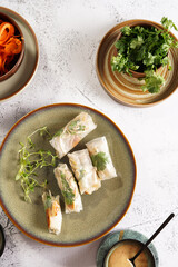 Several spring rolls with chicken, carrot and bamboo sprouts in rice paper on green plate, sesame sauce and coriander on concrete surface