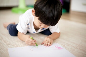 Little asian boy laying and drawing on paper : close up