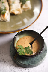 Creamy sesame sauce in a black dip bowl and coriander on a concrete surface
