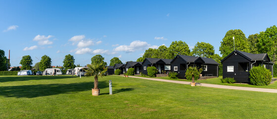panorama view of an idyllic campground in Denmark with little black glamping hosues and...